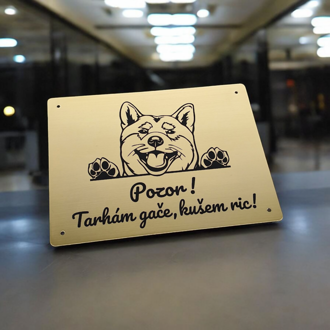 Zlatá tabulka s vykukující akitou inu a vtipným nářečním nápisem